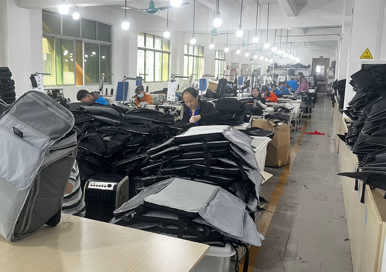 Active bag sewing workshop with operators assembling backpack panels across a production line